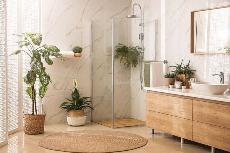 3/8” vs. 1/2” Shower Door Glass: What’s the Difference and Does It Matter? 1 corner frameless glass shower enclosure in a modern bathroom with marble walls and wood cabinetry